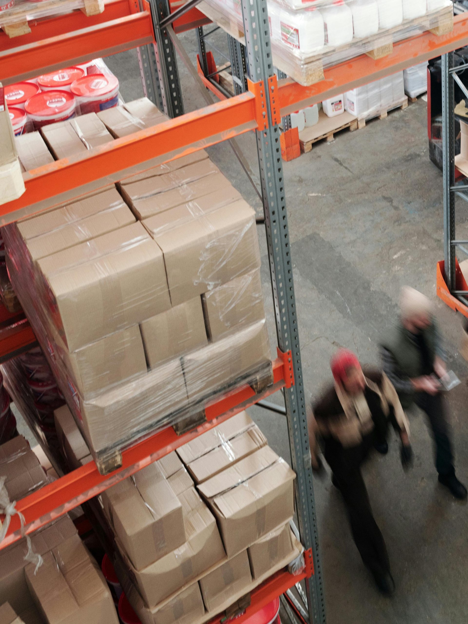 A high angle view of workers in motion in a busy warehouse with shelves full of boxes and packages.
